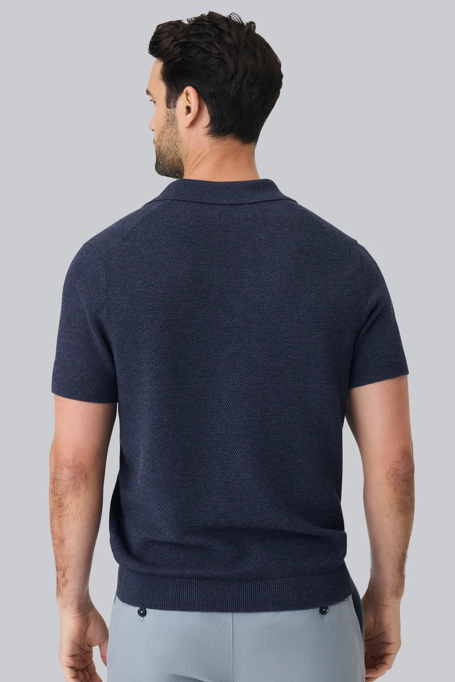 A man with short dark hair is seen from behind wearing the MACK WELDON Tech Linen Johnny Collar Polo Sweater in Sage Leaf Heather, paired with light gray pants against a plain light gray background.