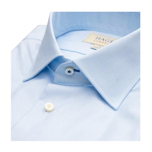 The HAGEN - COTTON DRESS SHIRT IN SKY MINI HOUNDSTOOTH features a modern spread collar, white buttons, and premium cotton fabric. The neatly folded shirt displays the Hagen label and comes in a light blue mini houndstooth pattern.