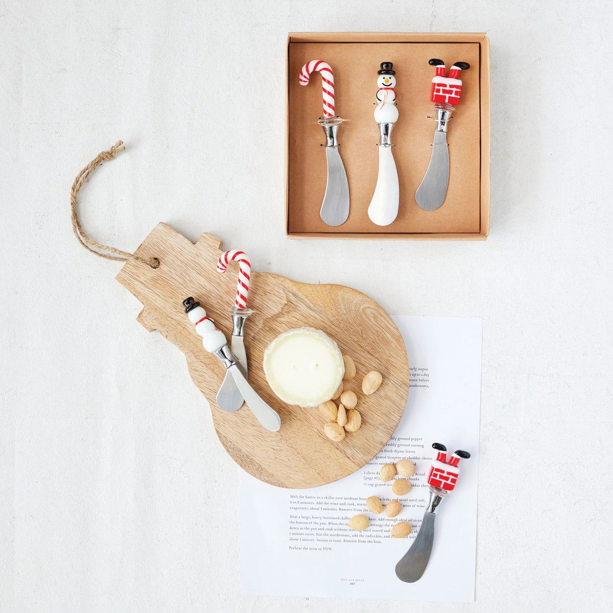The CREATIVE COOP CANAPE KNIVES WITH HOLIDAY MOTIF boxed set includes three stainless steel knives, each with a festive handle—a candy cane, snowman, and Santa’s legs—shown in the box and separately on a white background.