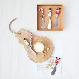 The CREATIVE COOP CANAPE KNIVES WITH HOLIDAY MOTIF boxed set includes three stainless steel knives, each with a festive handle—a candy cane, snowman, and Santa’s legs—shown in the box and separately on a white background.