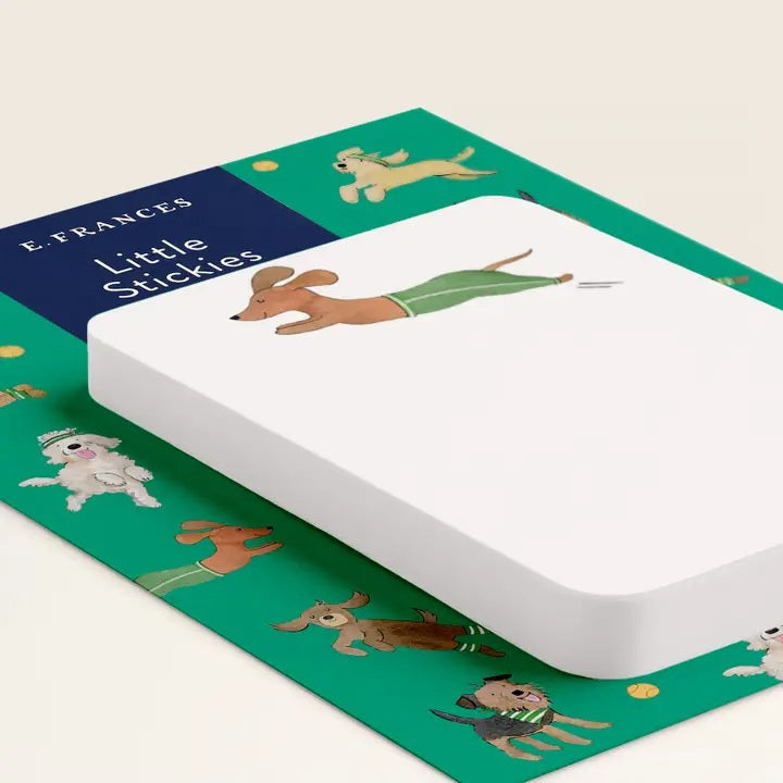 E. FRANCES PAPER's "Little Stickies Off Leash" notepad features a brown dachshund in green pants, with a backing card decorated with playful cartoon dogs on a green background—perfect dog stationery for any pup lover.