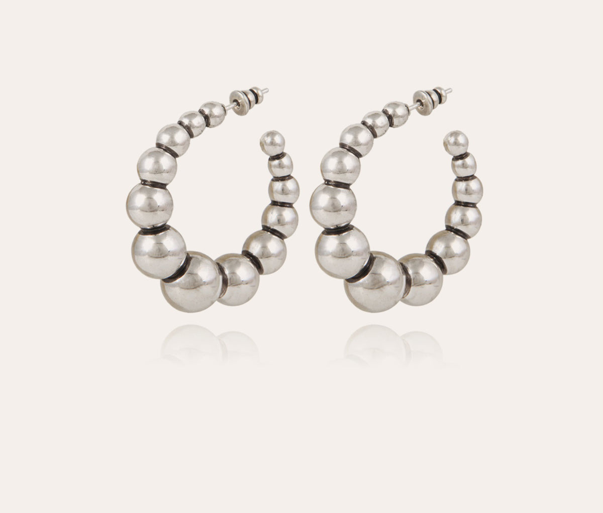 The GAS BIJOUX - ANDY SILVER HOOP EARRINGS feature a stunning design with graduated spheres, arranged from small to large and back to small. Their reflective surface offers a polished and sleek look akin to pearls set against a light background. These elegant silver-plated earrings are truly exquisite.