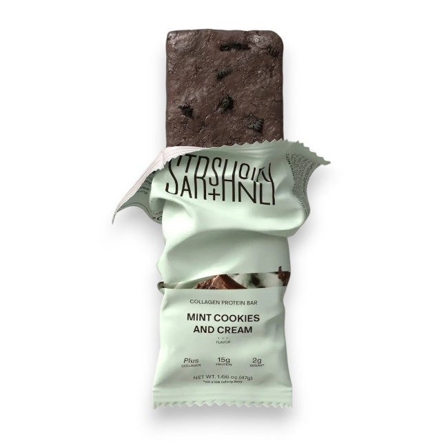 A STARS+HONEY - MINT COOKIES & CREAM Collagen Protein Bar, with its wrapper, displays mint chocolate ice cream and cookie pieces bursting out for a dynamic effect against a beige background.