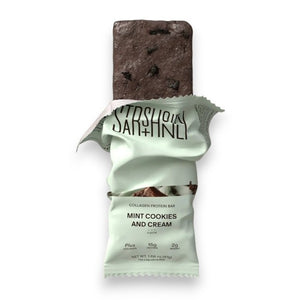 A STARS+HONEY - MINT COOKIES & CREAM Collagen Protein Bar, with its wrapper, displays mint chocolate ice cream and cookie pieces bursting out for a dynamic effect against a beige background.