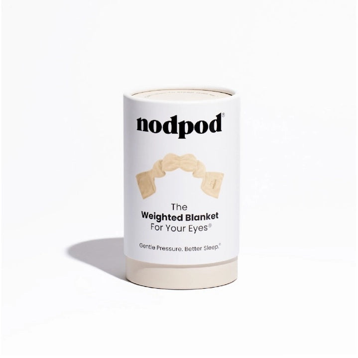 The NODPOD Weighted Sleep Eye Mask in Bone by NODPOD is a beige, segmented, plush mask with wider ends and a gently wavy, narrower middle section, shown laid flat on a white background—ideal for providing gentle pressure and soothing comfort as a weighted eye mask.