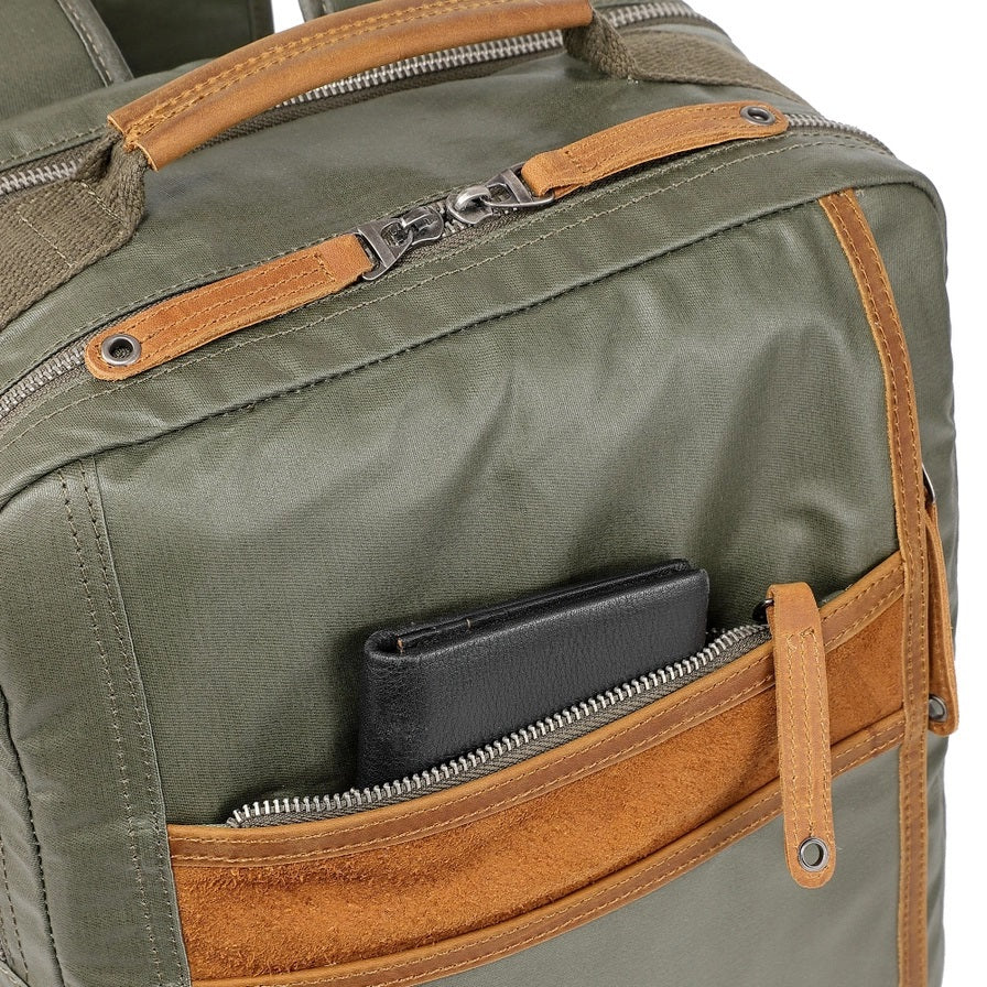 The TSD BRAND Madrone Coated Canvas Backpack in army green features brown leather accents, zippers, a top flap, side handles, metal rings, and a leather logo patch; shown lying flat to display these details.
