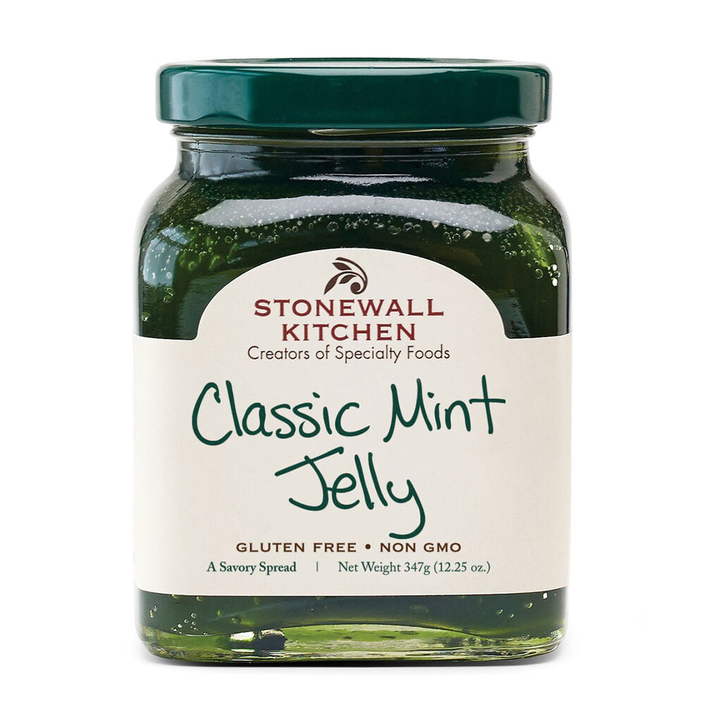 A jar of STONEWALL KITCHEN - CLASSIC MINT JELLY showcases a vibrant green jelly through its clear glass. The label proudly displays "Creators of Specialty Foods," "Gluten Free," and "Non GMO," indicating its quality ingredients. It weighs 347g (12.25 oz) and is topped with a dark green lid, making it an ideal accompaniment for lamb and other hearty meats.