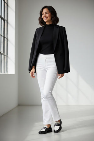 A woman stands in profile against a plain light background, wearing a black blazer draped over her shoulders, a black top, and the SPANX ON THE GO KICK FLARE pant—crafted with Ultimate Opacity Technology for comfort—paired with black loafers.