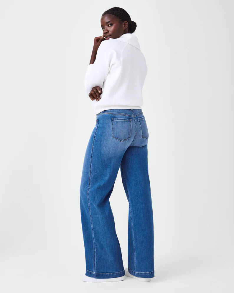 A person with short hair is wearing a SPANX AIRESSENTIALS HALF ZIP sweater in navy blue, made from lightweight spacer fabric, paired with black pants. Their arms are crossed over their chest as they stand against a plain, light grey background.