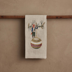 A beige linen DECK THE HALLS FOX LINEN TEA TOWEL embroidered with a fox holding a large, striped Christmas ornament, perfect for vintage Christmas kitchen decor.