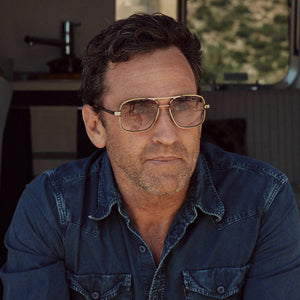 The CADDIS - METAMODERNIST SCOUT READERS by CADDIS are aviator-style sunglasses featuring a slim metal alloy frame and gradient, scratch-resistant lenses that fade from light blue to pink, displayed on a white background.