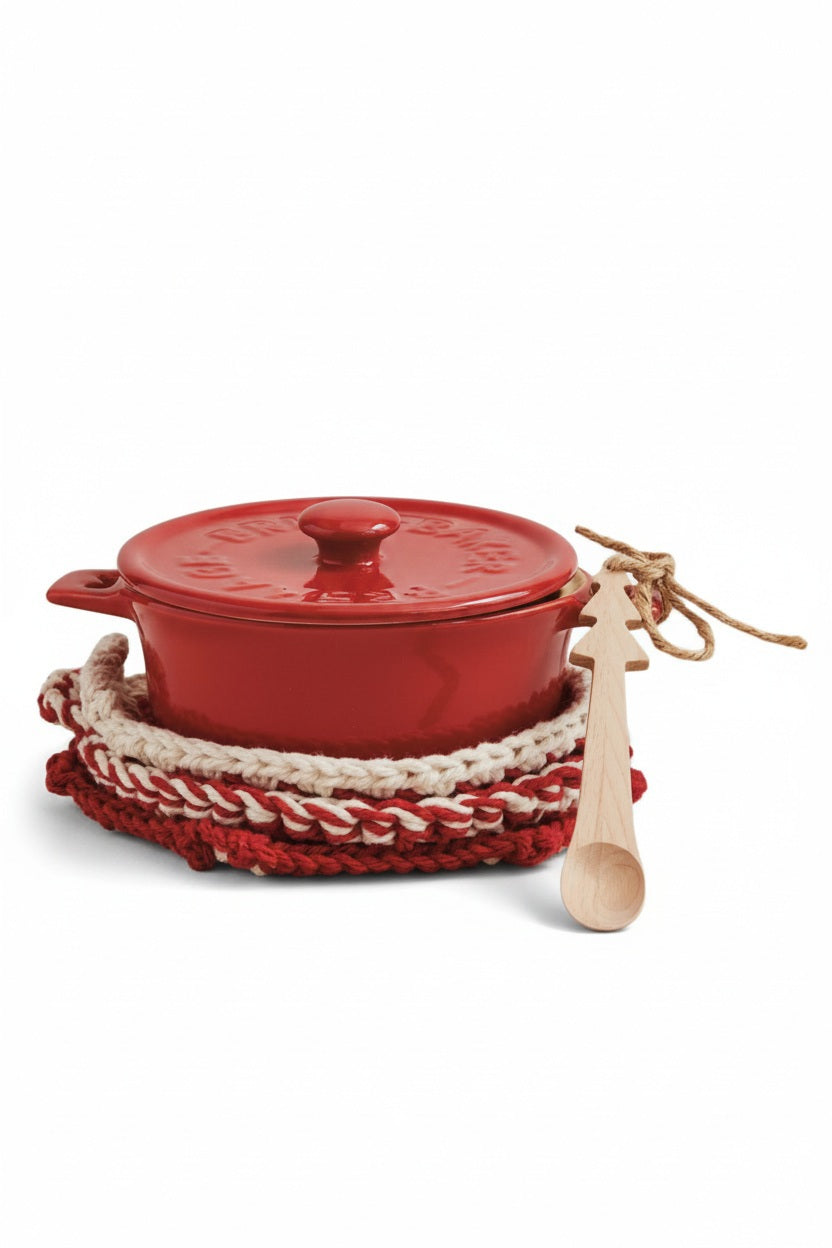 The CREATIVE COOP STONEWARE BRIE BAKER WITH BAMBOO TREE SPOON sits atop red and white pot holders, its lid angled nearby, with a spoon tied in twine on a beige fabric surface against a textured light wall.