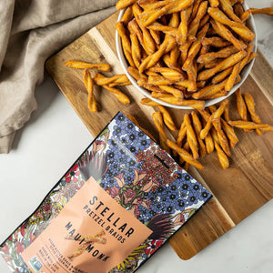 A vibrant 5oz bag of STELLAR SNACKS - MAUI MONK PRETZEL BRAIDS, adorned with lively floral artwork. The packaging showcases vegan butter braids seasoned with Maui onion and monk fruit, standing out as a delicious Non-GMO vegan snack. Experience the perfect crunch of these Maui onion pretzel braids, proudly made in the USA by STELLAR SNACKS.