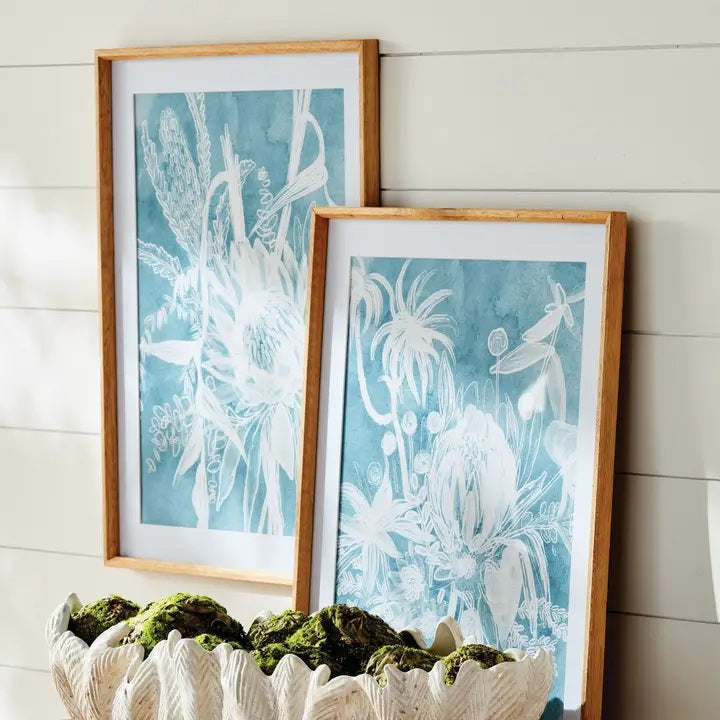A framed protea abstract print in soft blue by NAPA HOME AND GARDEN, featuring a white floral illustration on a blue background. This botanical wall art is presented in a light wood frame for a fresh, contemporary look—perfect for modern home décor.