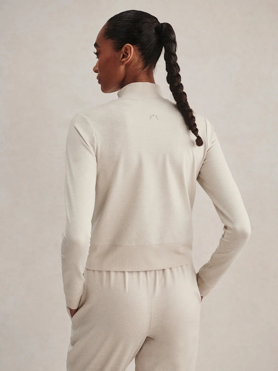 A person wears a light beige Varley Rufus Cropped Zip Through Sweat in Pebble Marl with a high collar and matching pants.