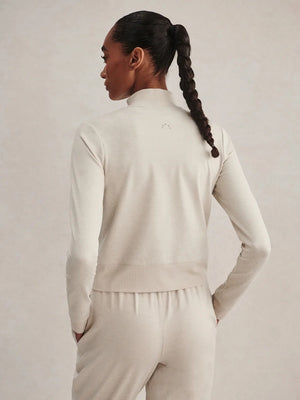 A person wears a light beige Varley Rufus Cropped Zip Through Sweat in Pebble Marl with a high collar and matching pants.