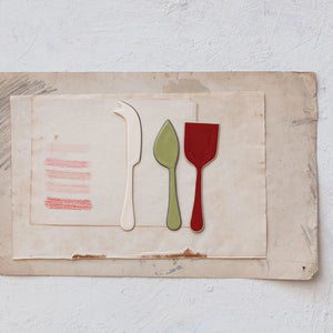 The CREATIVE COOP ENAMELED STAINLESS STEEL CHEESE SERVERS - SET OF 3 includes a fork-tipped cheese knife, flat-bladed spatula, and pointed server with colorful handles, shown on a white background.