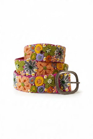 The JENNY KRAUSS WILDFLOWERS EMBROIDERED WOOL BELT features hand-embroidered floral patterns in orange, yellow, green, purple, and white on a peach background, crafted in Peru with a silver buckle and shown coiled on a white surface.