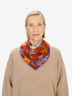 Fearrington Village Inoui Editions Toutou wool scarf in orange with floral print worn by a woman