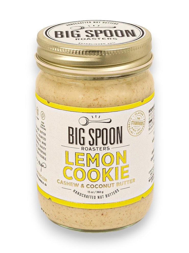 A jar of Big Spoon Roasters Cashew Lemon Coconut Nut Butter sits with a gold lid and a white label adorned with yellow accents. The label features the product name, brand logo, and highlights that this cashew butter is sweetened with coconut nectar and handcrafted from natural ingredients.