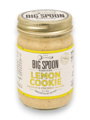 A jar of Big Spoon Roasters Cashew Lemon Coconut Nut Butter sits with a gold lid and a white label adorned with yellow accents. The label features the product name, brand logo, and highlights that this cashew butter is sweetened with coconut nectar and handcrafted from natural ingredients.
