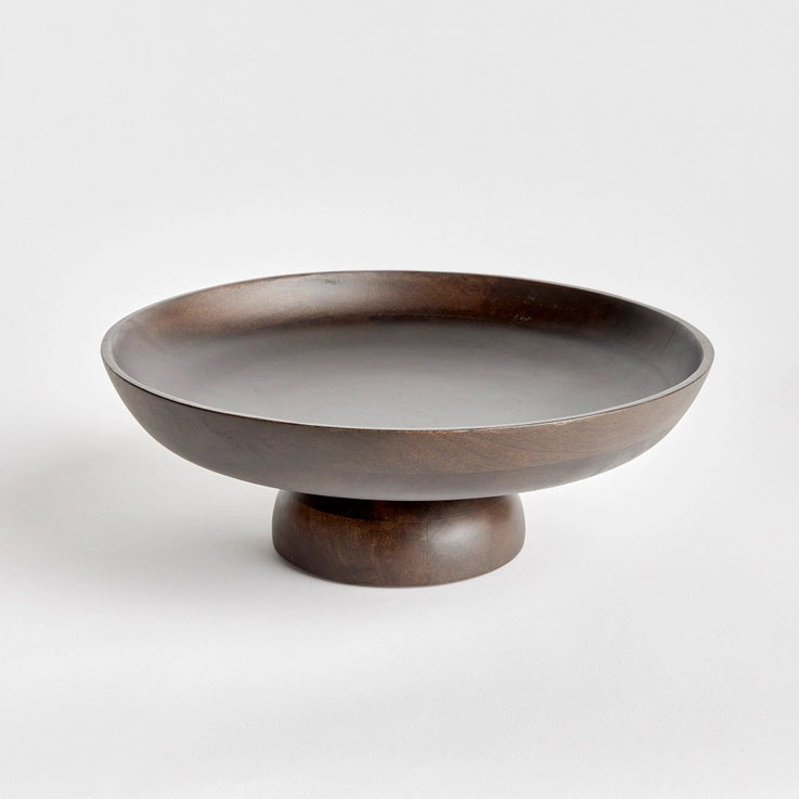 The NAPA HOME AND GARDEN - BOWIE FOOTED BOWL features a dark mango wood pedestal design with a wide, shallow bowl and sturdy base. Its smooth finish showcases natural grain patterns, merging classic craftsmanship with contemporary style against a plain white background.