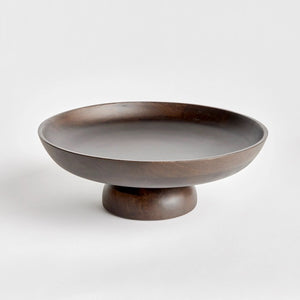 The NAPA HOME AND GARDEN - BOWIE FOOTED BOWL features a dark mango wood pedestal design with a wide, shallow bowl and sturdy base. Its smooth finish showcases natural grain patterns, merging classic craftsmanship with contemporary style against a plain white background.