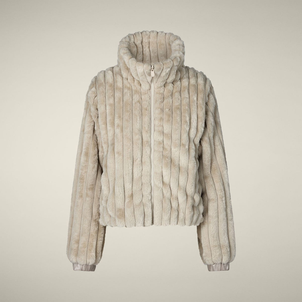 A woman models the SAVE THE DUCK - ELINA REVERSIBLE JACKET in beige fur, styled with a white skirt, orange tights, burgundy boots, and a matching clutch, standing against a plain light background.