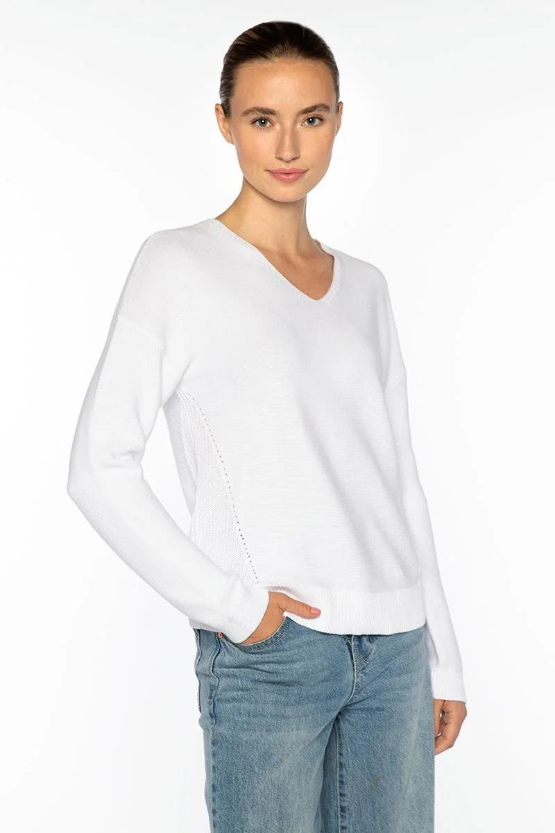 A woman with brown hair pulled back wears the KINROSS CASHMERE MICRO GARTER EASY VEE NECK COTTON SWEATER in white and blue jeans. She stands against a plain white background, one hand in her pocket, smiling slightly at the camera.