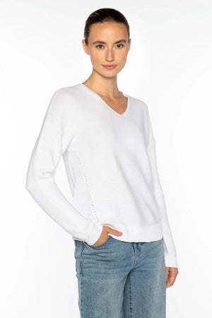 A woman with brown hair pulled back wears the KINROSS CASHMERE MICRO GARTER EASY VEE NECK COTTON SWEATER in white and blue jeans. She stands against a plain white background, one hand in her pocket, smiling slightly at the camera.