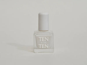 A glass bottle of TENOVERTEN - NAIL POLISH from the brand TEN OVER TEN, featuring a white cap and a dusty pink nail color. The front label displays "TEN OVER TEN" in white uppercase letters. This vegan, eight-free formula ensures both beauty and peace of mind. The background is plain and light-colored.