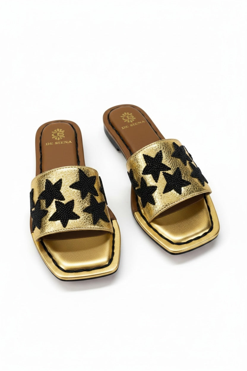The DE SIENA DA SIENA - BEADED STARS SLIDES are brown and gold metallic open-toe leather slides with a wide strap featuring black beaded star designs and a gold insole outlined in brown with "DE SIENA" branding near the heel.