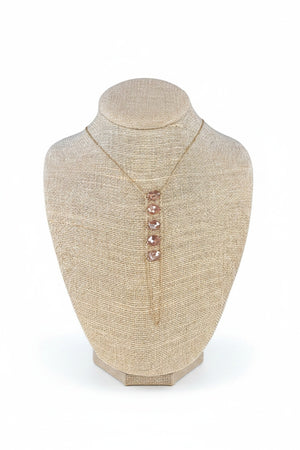 The GOLDISH - LADDERS TO BLISS PINK MOONSTONE NECKLACE features a gold vertical pendant with five pink moonstones, displayed on a beige textured bust against a white background, representing balance and harmony from GOLDISH.