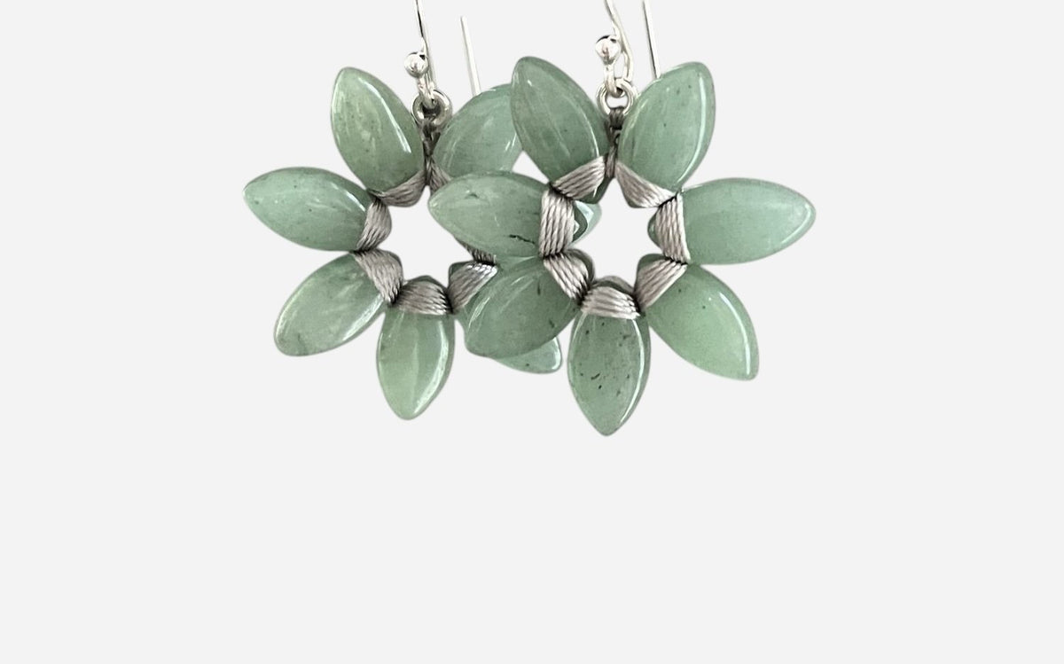 The ANN LIGHTFOOT - SEVEN PETAL AVENTURINE FLOWER EARRINGS feature aventurine stones in a floral design on sterling silver hooks. Each earring has three green stones wrapped in delicate silver wire, creating an elegant contrast against a plain white background.