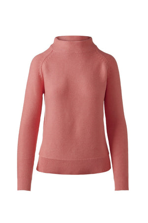 A woman with long brown hair pulled back wears the KINROSS CASHMERE Garter Funnel Cotton Sweater in Coral by KINROSS, paired with white pants against a plain white background—a stylish, breathable, and versatile wardrobe choice.