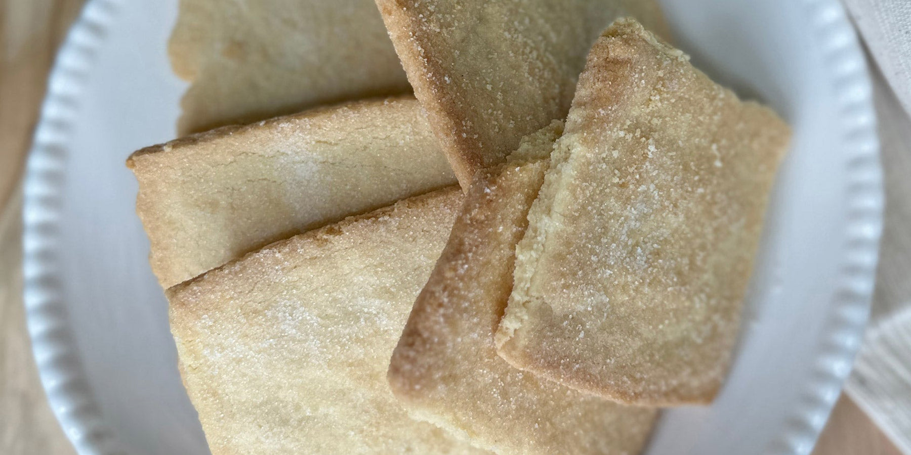 A white plate with several rectangular, golden-brown shortbread cookies sprinkled lightly with sugar.