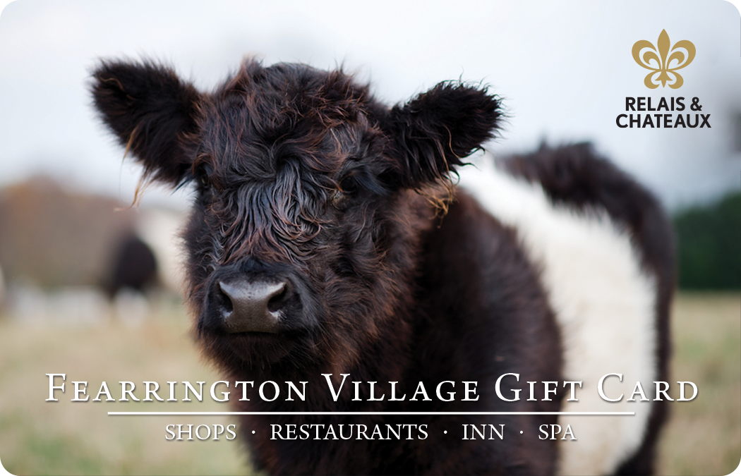 A close-up of a black and white cow standing in a field, with the text "Fearrington Village Gift Card" and "Shops · Restaurants · Inn · Spa" alongside the Relais & Chateaux logo in the top right corner.