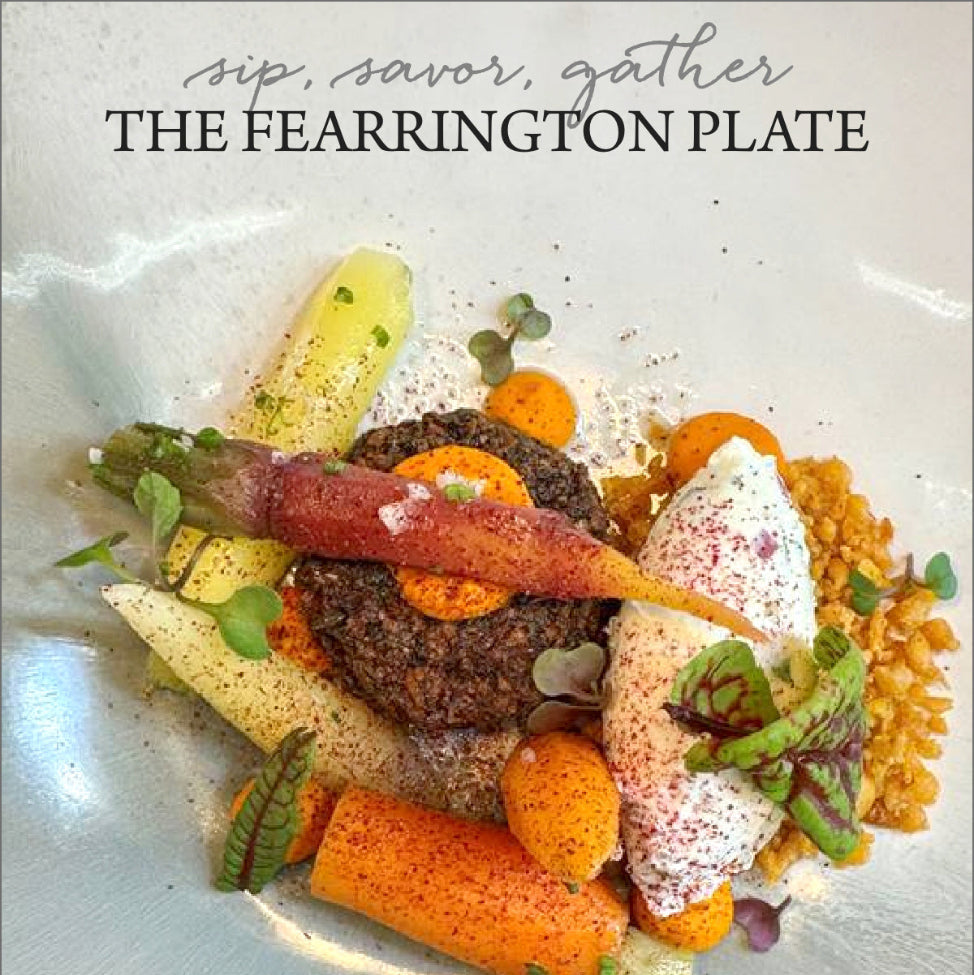 A gourmet dish with colorful carrots, a round patty, a dollop of cream, microgreens, and grains, artfully arranged on a white plate. Text above reads: “sip, savor, gather THE FEARRINGTON PLATE.”.