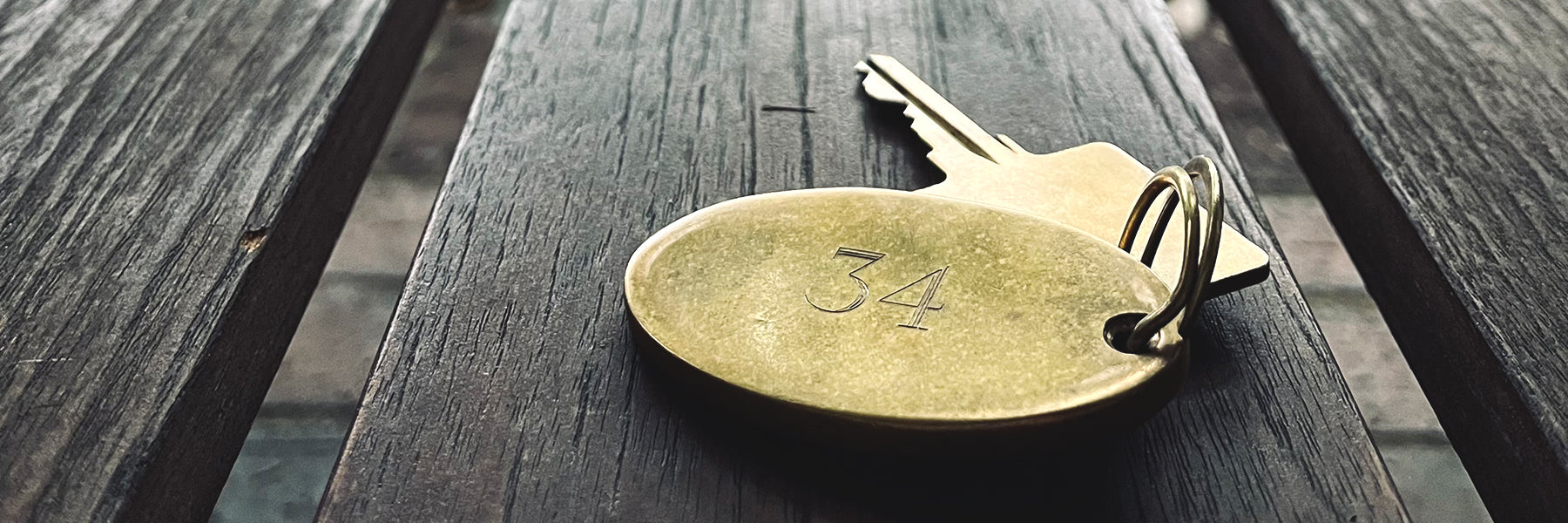 A gold-colored key tag stamped with the number 34 and an attached key rest on a dark wooden surface.