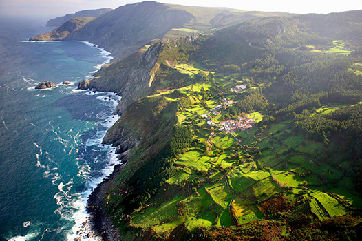 Aerial view of Spain’s rugged coastline, where steep cliffs and green hills meet the blue ocean—home to vineyards featured in FEARRINGTON VILLAGE's Wine Class: Spanish Coastlines - Under the Sea's Influence.