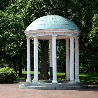 A small, white, round gazebo with a domed roof supported by eight columns, surrounded by greenery and trees in an outdoor setting.
