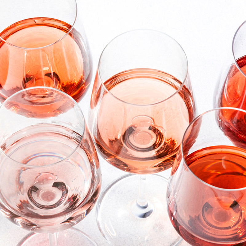 Several glasses filled with varying shades of rosé and red wine are arranged on a white surface, creating a colorful and elegant overhead view.