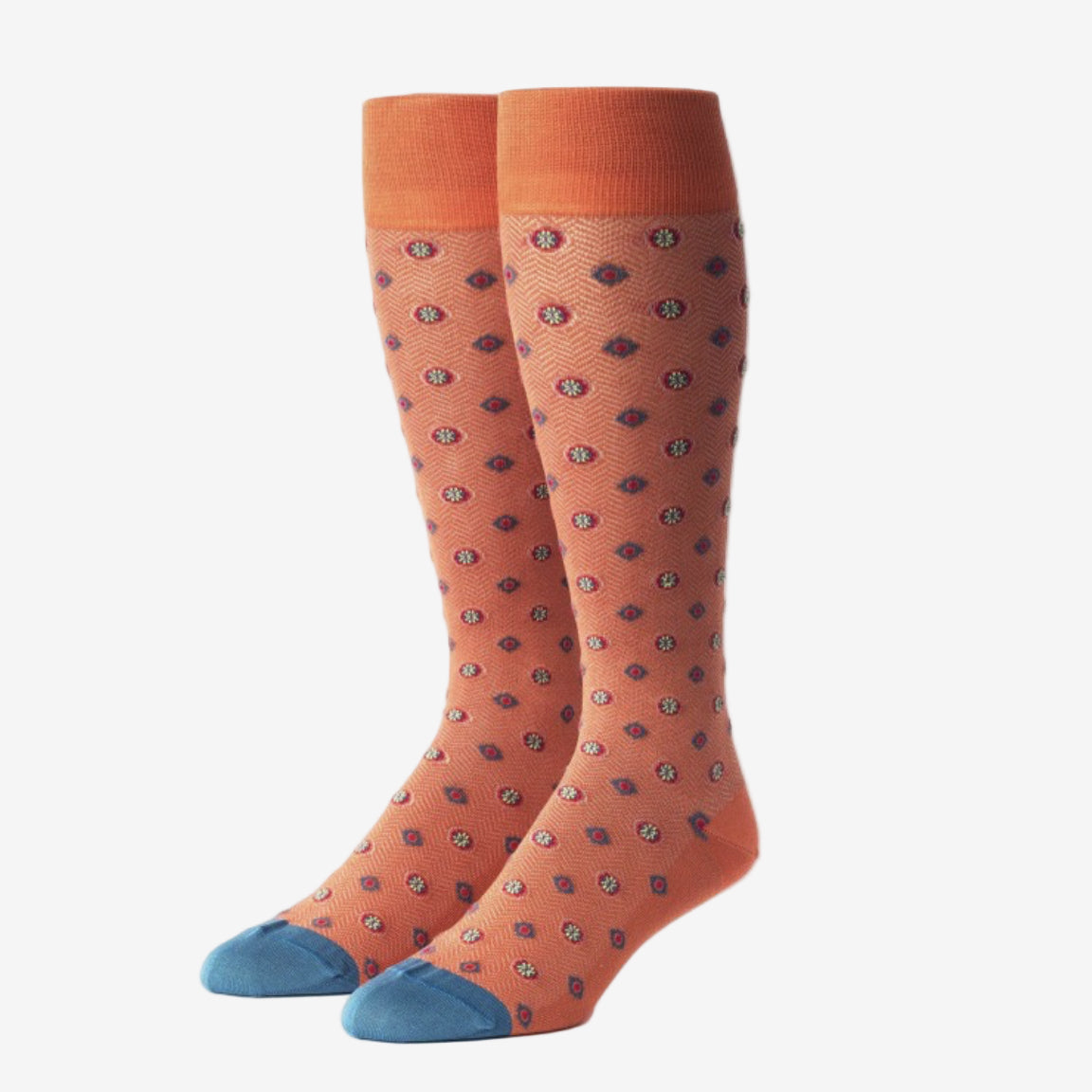 A pair of knee-high orange socks with a repeating small blue and red circular pattern, featuring solid orange cuffs and blue toes.