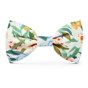 The DOG BOW TIE (STANDARD, GATHERED) by THE FOGGY DOG showcases a colorful floral pattern on a white background, featuring green leaves and flowers in shades of red, orange, and yellow. This vibrant and cheerful accessory is handcrafted in the USA, making it a perfect addition to your dog's accessories collection.