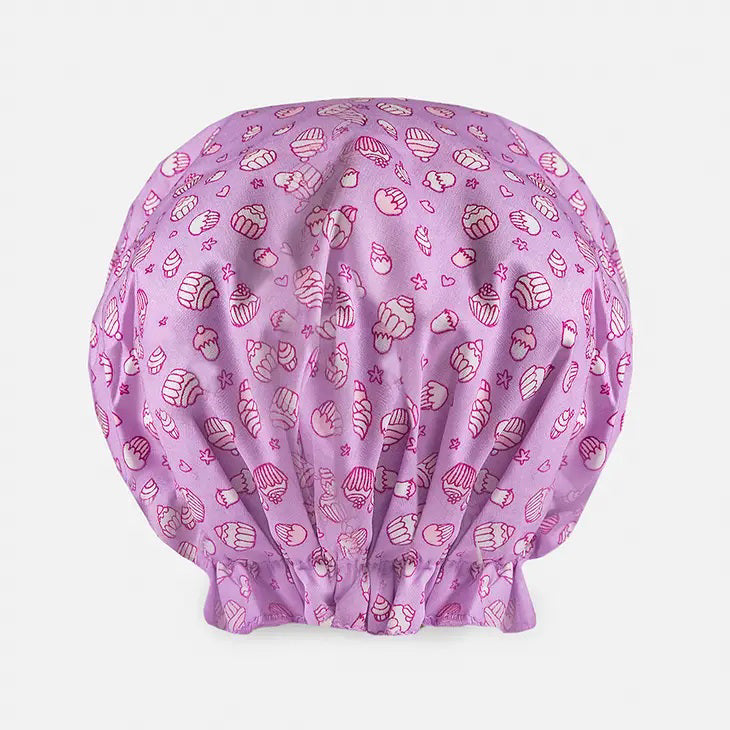 Introducing the BOUFFANT SHOWER CAP from BATH ACCESSORIES COMPANY! This stylish shower cap showcases a vibrant design of colorful macarons in shades of pink, purple, yellow, and brown against a lively green background. It features a waterproof inner layer to keep your hair dry and an elasticated bottom for a secure and comfortable fit.
