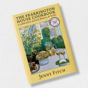 Yellow cookbook titled "The Fearrington House Cookbook" by Jenny Fitch, featuring an illustrated cover of a garden scene with a table set with food, wine, and flowers, subtitled “a celebration of food, flowers, & herbs.”.