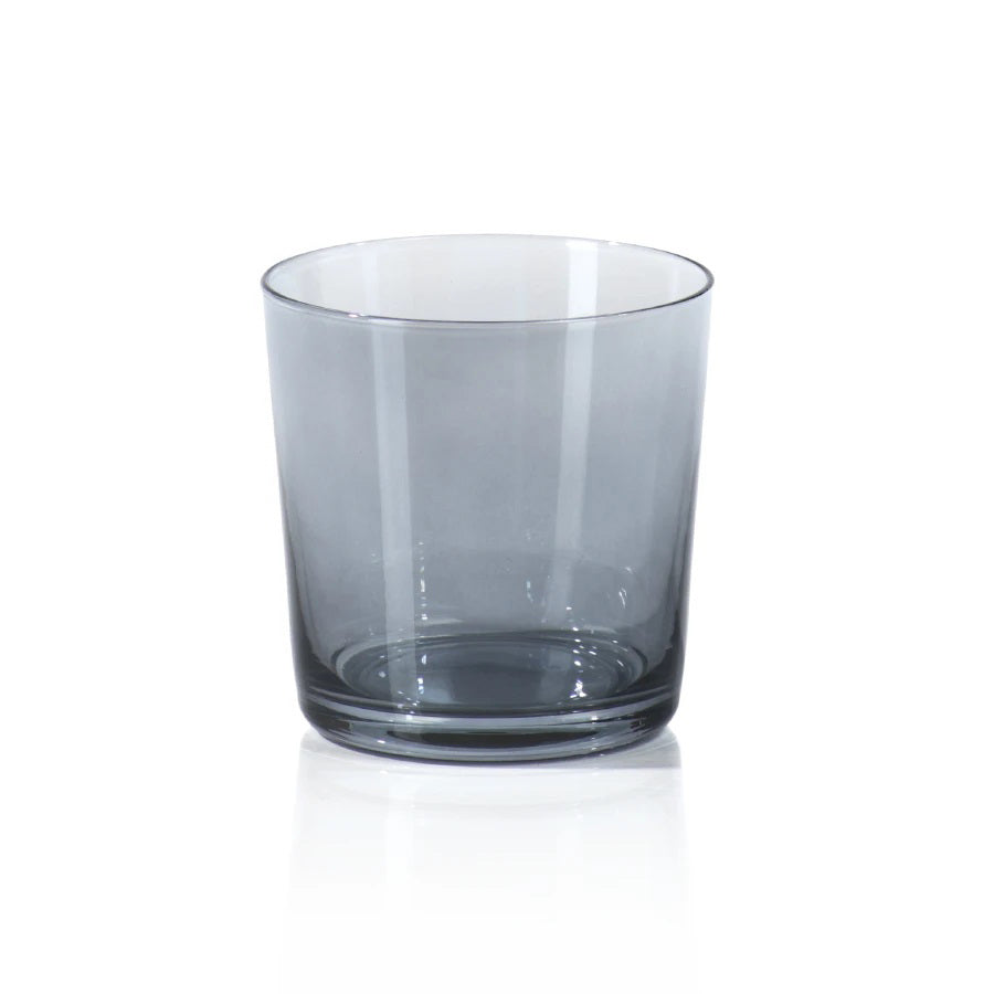 A clear, empty GREY LUSTER ROCKS GLASS from ZODAX, with dimensions of 3.75 in x 3.75 in and a slightly tapered base, is placed on a plain white surface. The glass has a modern, simple design and is recommended as handwash only.