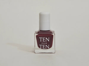 A glass bottle of TENOVERTEN - NAIL POLISH from the brand TEN OVER TEN, featuring a white cap and a dusty pink nail color. The front label displays "TEN OVER TEN" in white uppercase letters. This vegan, eight-free formula ensures both beauty and peace of mind. The background is plain and light-colored.
