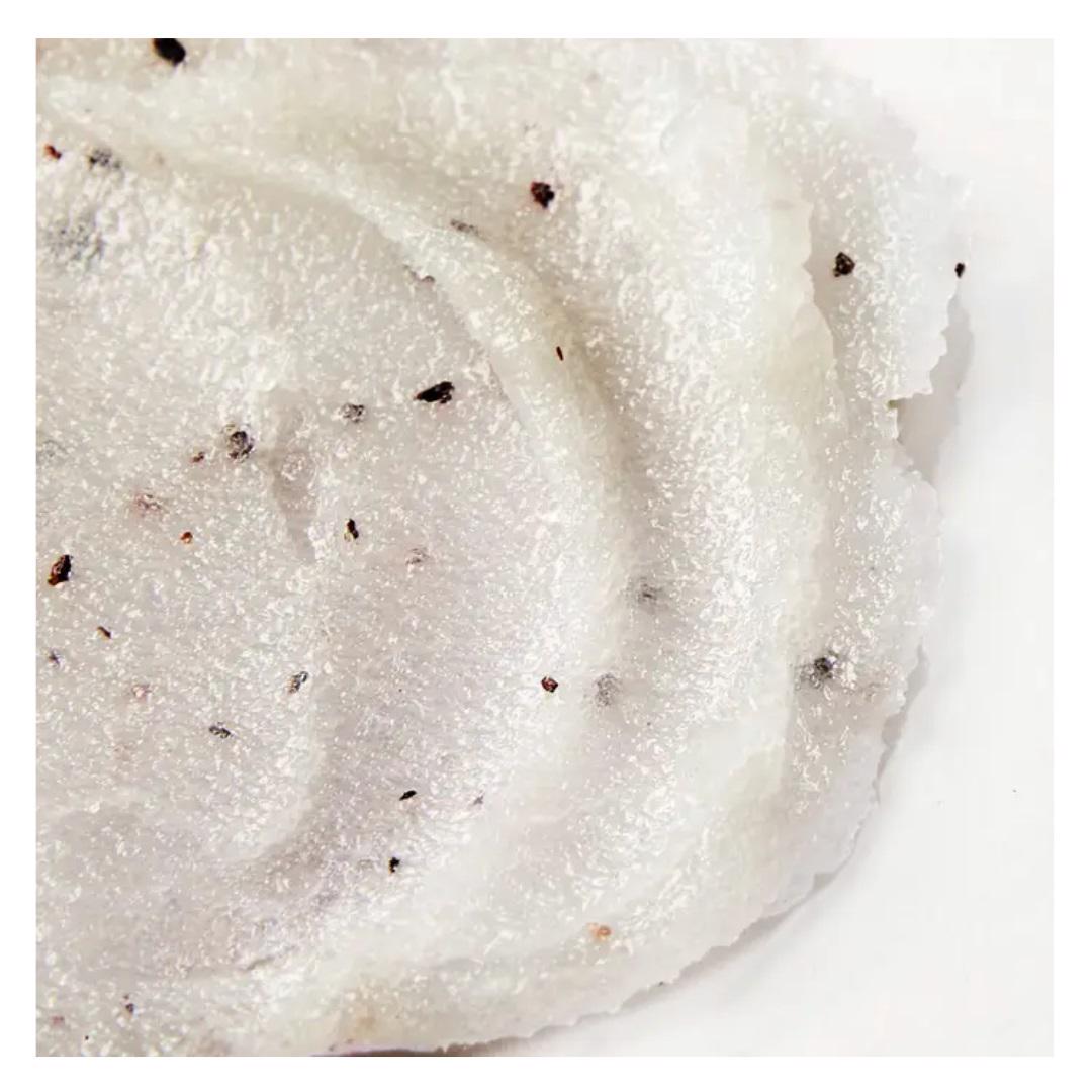 A jar of ELEMIS - FRANGIPANI MONOI SALT GLOW from ELEMIS - STEINER, containing 490 grams (17 ounces) of product. The jar has a white lid secured with a metal latch and is filled with a white, speckled exfoliating salt scrub enriched with Tahitian Monoi Oil. The label on the jar is red and provides product details.