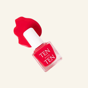 A glass bottle of TENOVERTEN - NAIL POLISH from the brand TEN OVER TEN, featuring a white cap and a dusty pink nail color. The front label displays "TEN OVER TEN" in white uppercase letters. This vegan, eight-free formula ensures both beauty and peace of mind. The background is plain and light-colored.